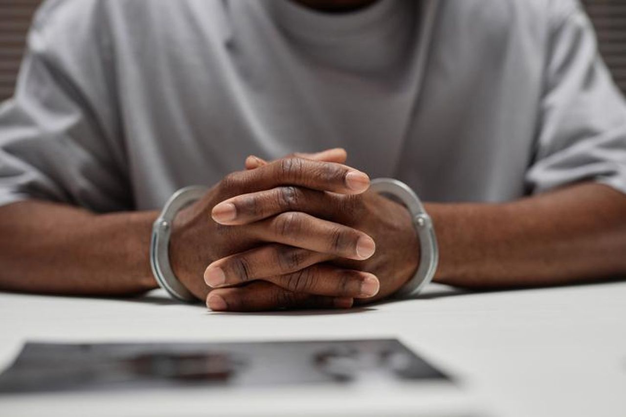 Accuse_contro_il_sindaco_di_Bogalusa_Smh7X97w46 - Confidenze24 source:bossip - Accuse contro il sindaco di Bogalusa - Primo piano di un uomo di colore con le manette seduto a un tavolo nel dipartimento di polizia