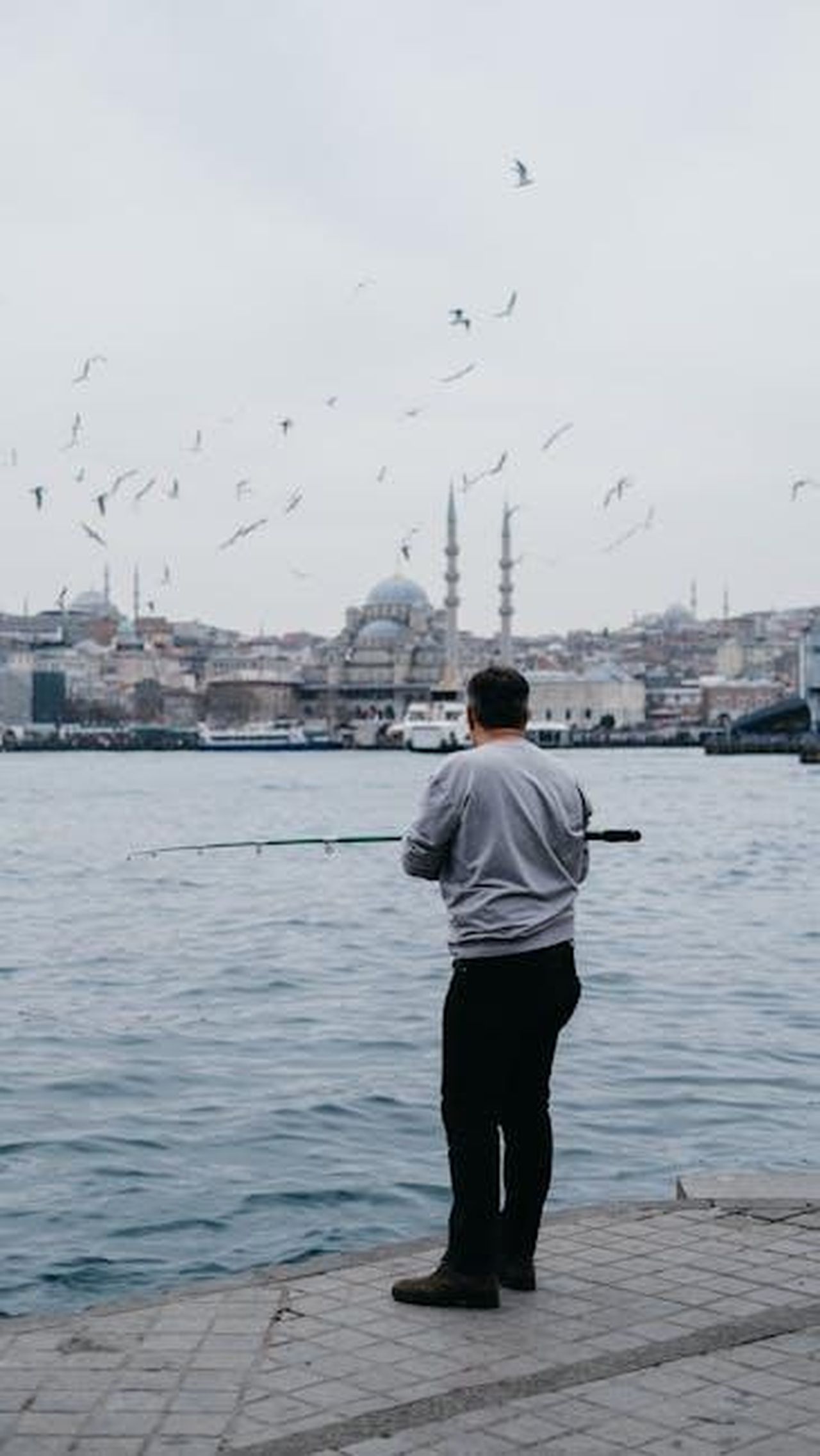 2_Ariete___Carica_e_passione_8yNu1OMfxf - Confidenze24 Source: Bilakis - pexels - A man fishing by the sea with a cityscape of Istanbul, Turkey in the background.