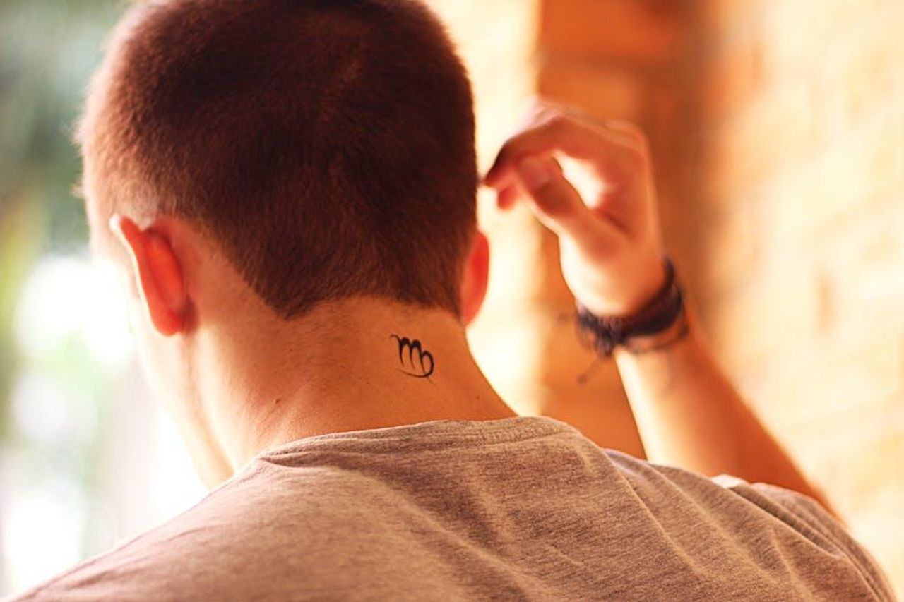 3_Acquario___Idee_vincenti_u3ZQ0mWkp1 - Confidenze24 Source: Carolina Almeida - pexels - A man with a tattoo on his neck adjusts his hair, captured from the back view in a warm, casual setting.