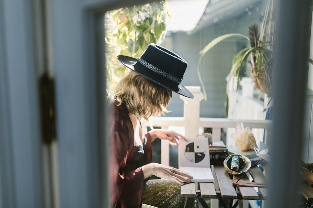 3_Sagittario_v556eFZsaD - Confidenze24 Source: RDNE Stock project - pexels - A woman in a hat reading tarot cards on a sunlit balcony surrounded by crystals.
