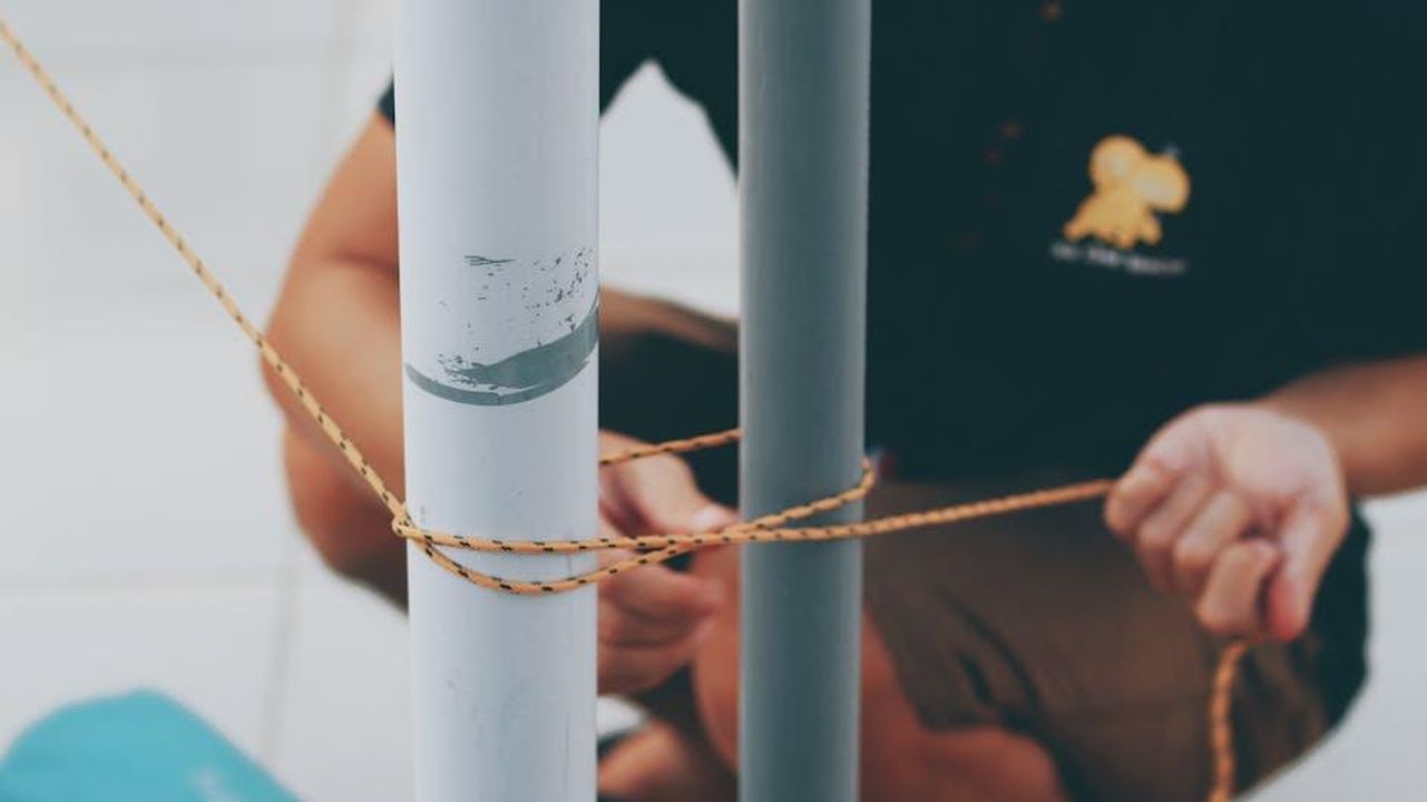 4_Toro_consolidamento_e_sicurezza_CXBTjsMezx - Confidenze24 Source: Bich Tran - pexels - Close-up view of hands tying rope around two metal posts, showcasing knot craftsmanship.