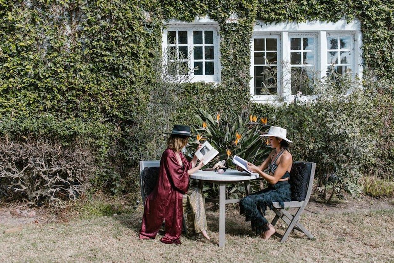 7_Gemelli_18SNmGZAha - Confidenze24 Source: RDNE Stock project - pexels - Two women in hats reading outdoors, surrounded by lush greenery and a serene garden atmosphere.