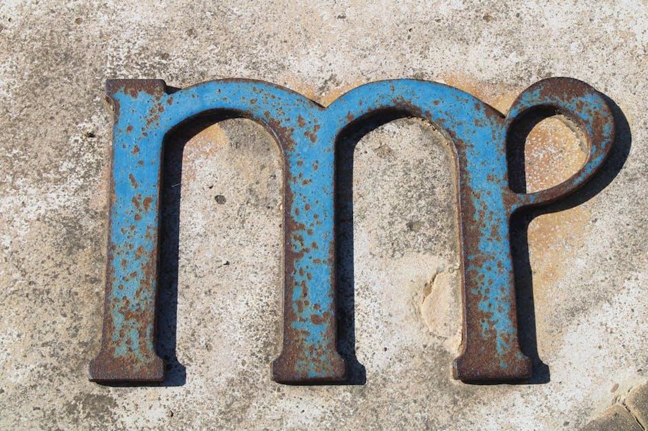 7_Vergine___Organizzazione_e_successi_47ZEqypT9h - Confidenze24 Source: Antonio Garcia Prats - pexels - Close-up of a rusty, blue metal letter on a textured concrete background, showcasing decay and texture.