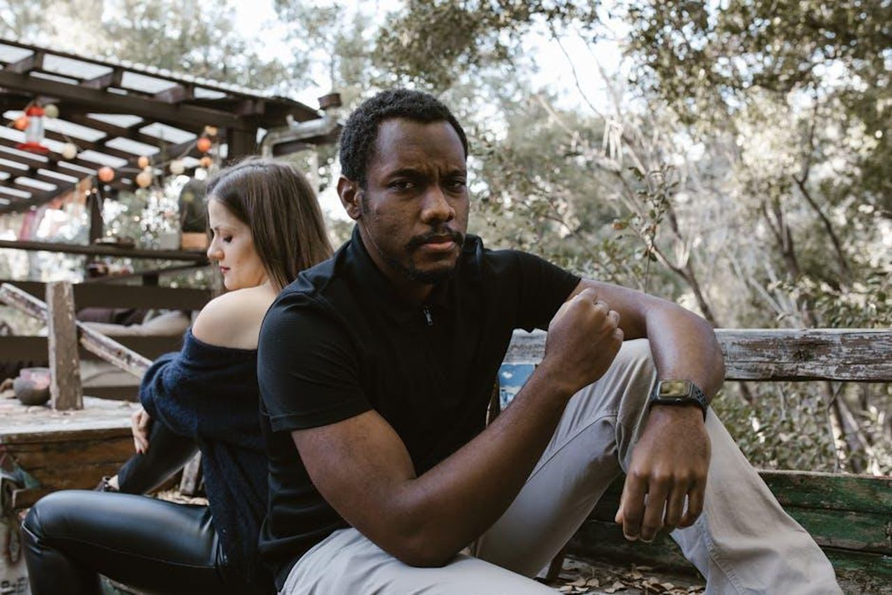 9_Ariete_tensioni_e_chiarimenti_necessari_1byYc6Yif5 - Confidenze24 Source: RDNE Stock project - pexels - A thoughtful man sits outdoors, with a woman sitting distantly behind him.
