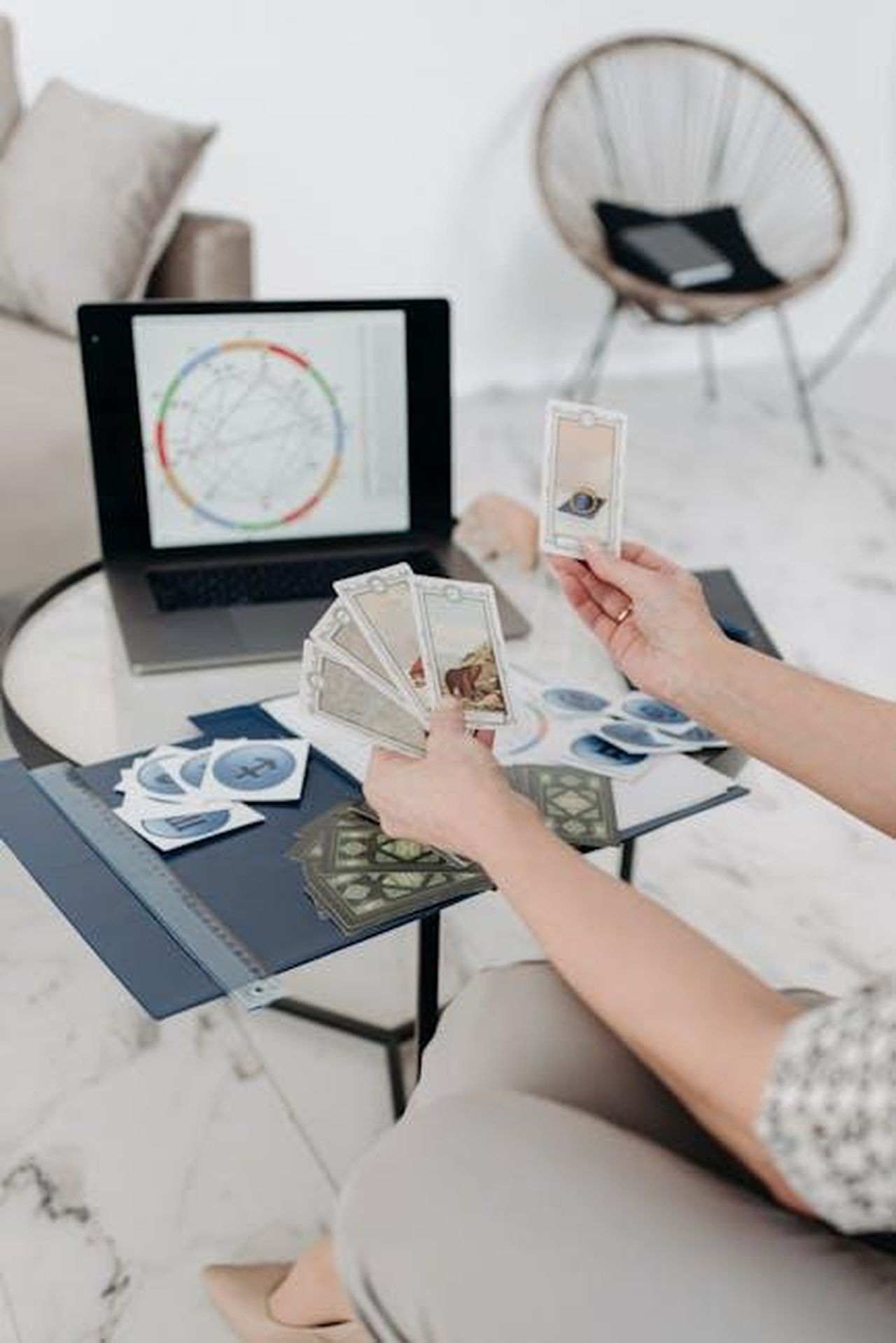 9_Scorpione_cj2XqdwRAZ - Confidenze24 Source: Pavel Danilyuk - pexels - A woman reads tarot cards at a table with a laptop displaying an astrology chart in a modern living room setting.