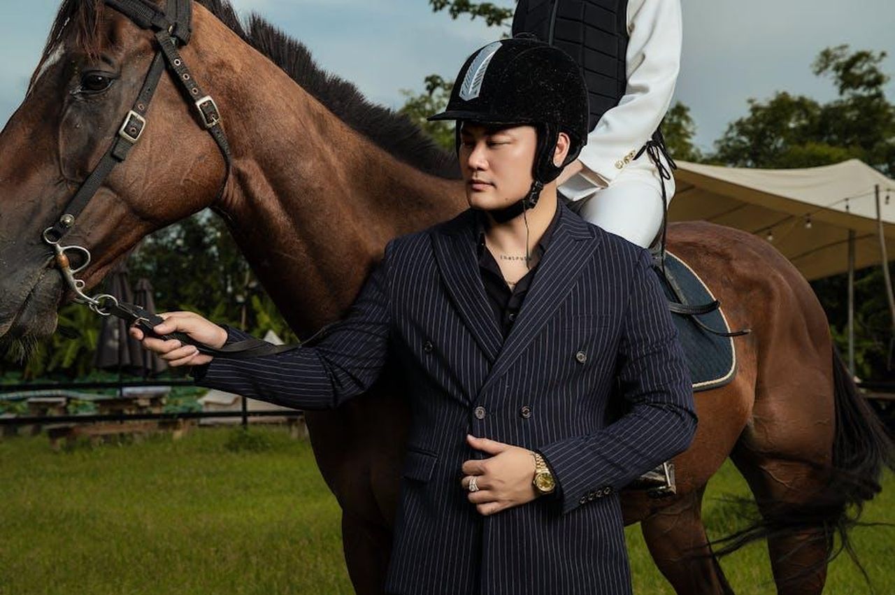 AAP_Rocky_esprime_ammirazione_per_RayBan_prima_della_nuova_partnership_kvibcws5YG - Confidenze24 Source: Đậu Lu - pexels - A stylish man in a suit holds a horse while another person rides it outdoors.
