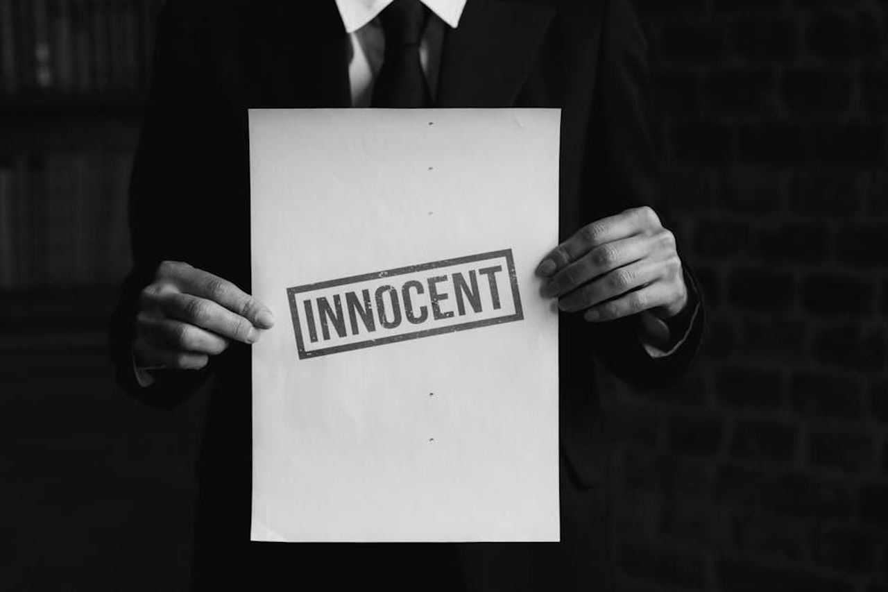 Accuse_contro_Gino_DAcampo_JijIZzVul7 - Confidenze24 Source: KATRIN BOLOVTSOVA - pexels - A black and white photo of a person holding a paper with 'INNOCENT' text, conveying a message of legal or moral purity.