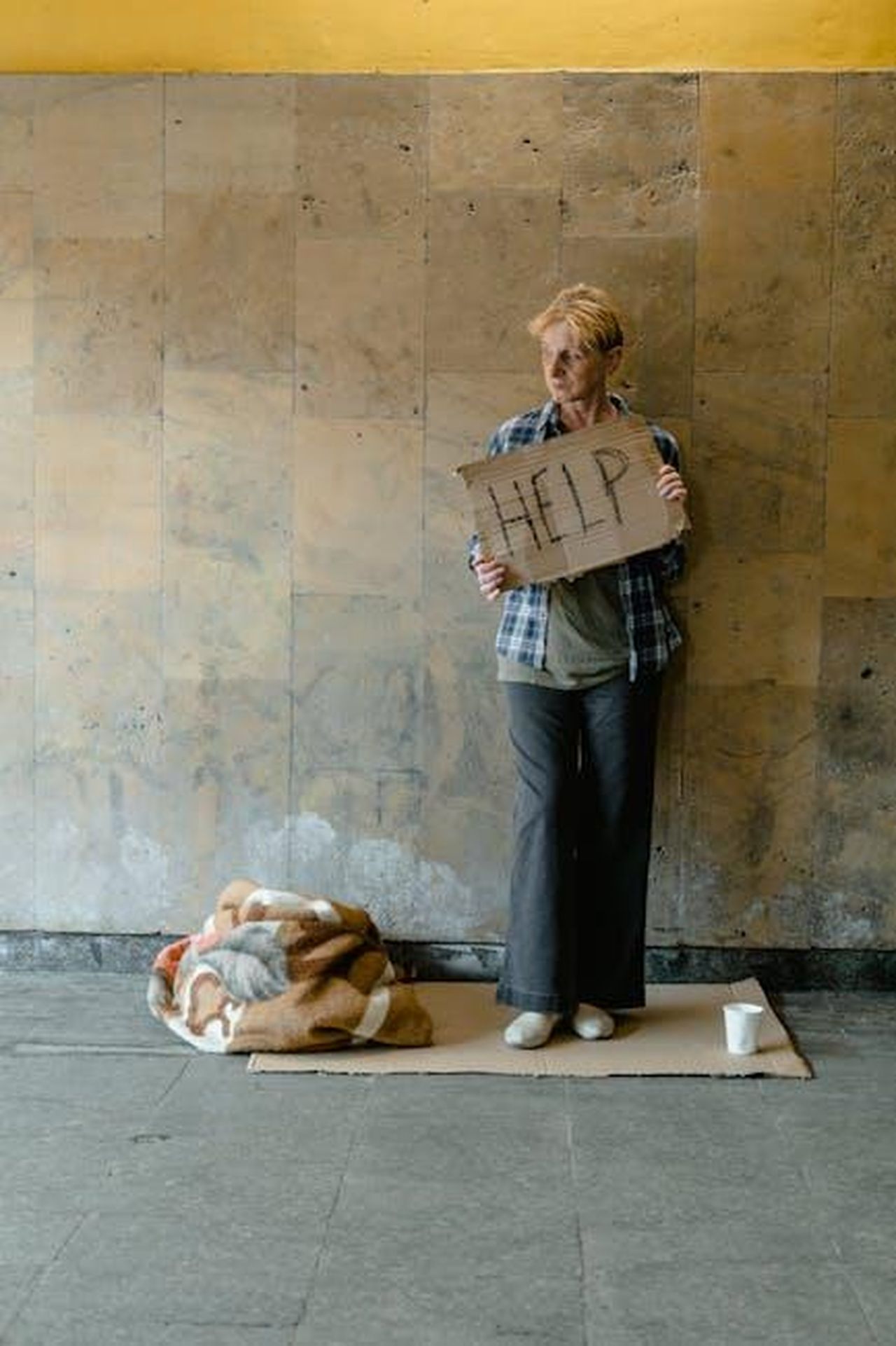 Accuse_e_cambiamento_di_percezione_E8iAdnQq4w - Confidenze24 Source: MART PRODUCTION - pexels - An elderly woman stands holding a cardboard sign that reads 'HELP,' conveying a sense of homelessness and need.