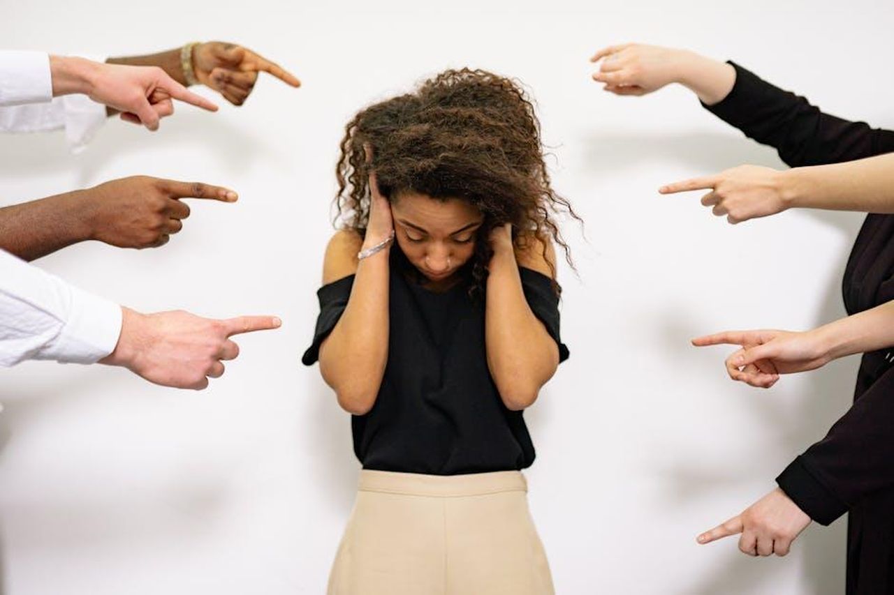Accuse_e_malintesi_7romcxteMZ - Confidenze24 Source: Yan Krukau - pexels - A young woman with curly hair looks distressed as multiple hands point accusatory fingers at her.