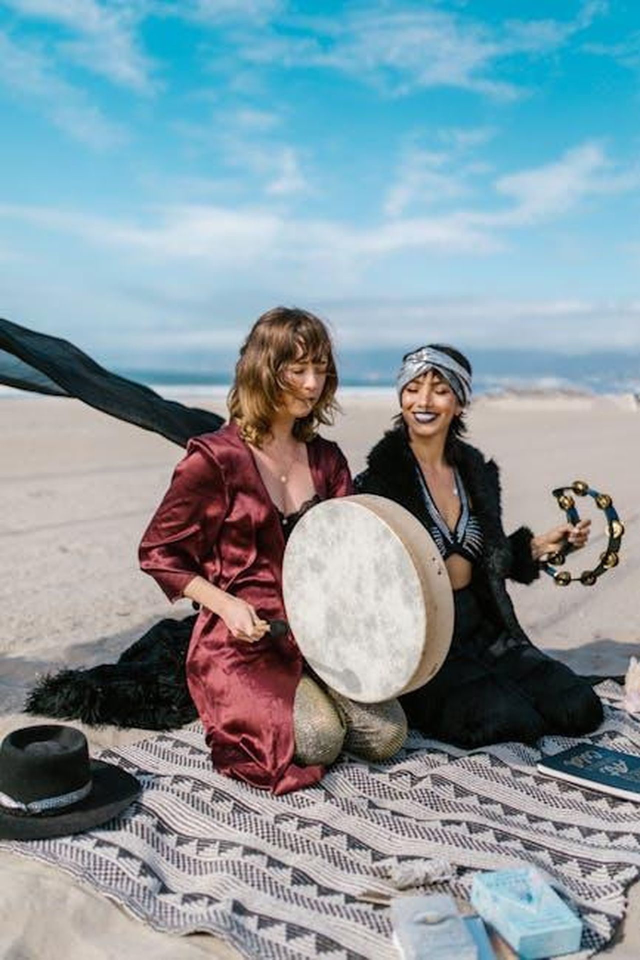 Acquario_attenzione_ai_litigi_wRlP9hmNwF - Confidenze24 Source: RDNE Stock project - pexels - Two women playing drums on the beach in a spiritual setting under a bright blue sky.