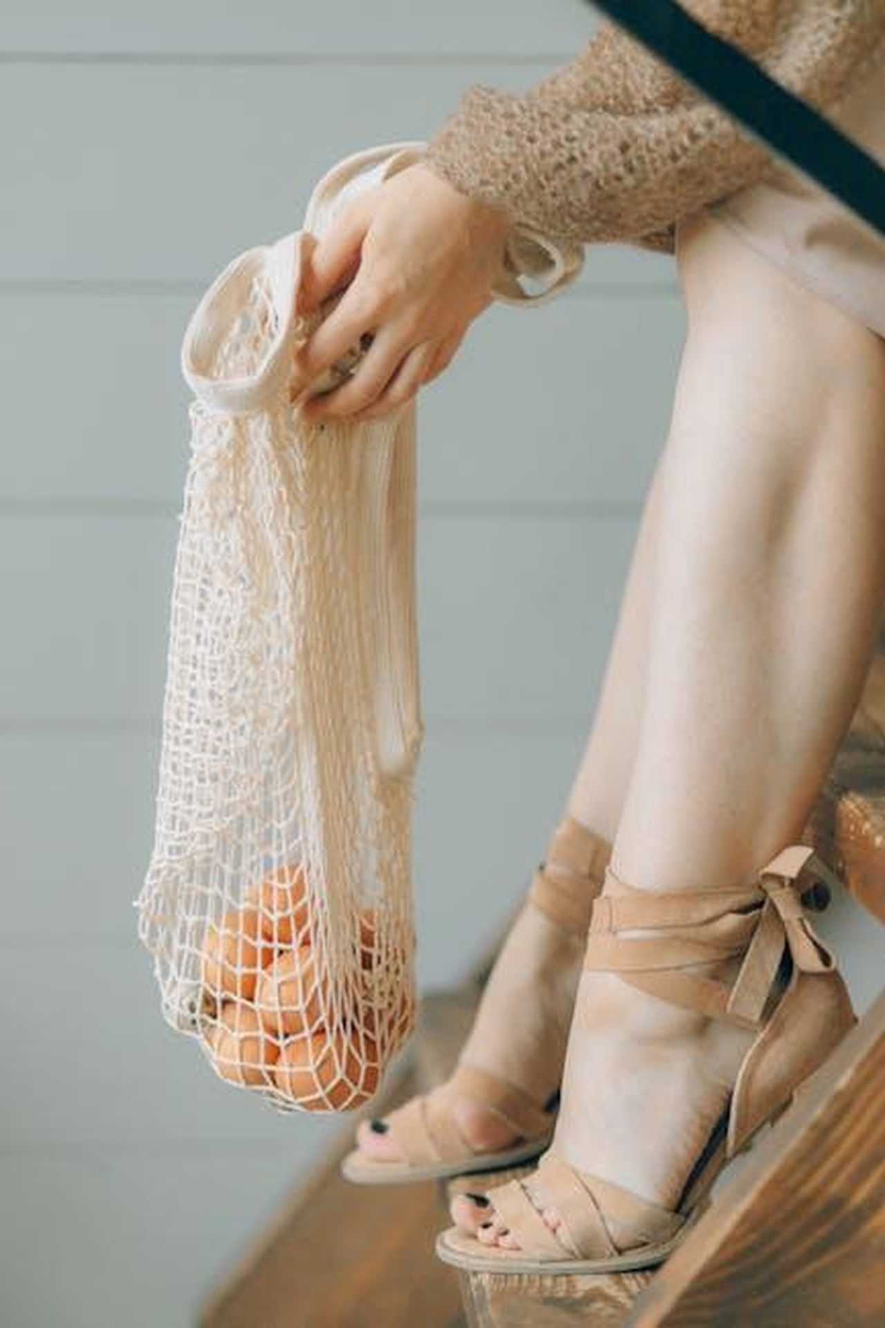 Acquisto_e_disponibilit_s09F3LQbbf - Confidenze24 Source: Nataliya Vaitkevich - pexels - Elegant woman sitting on stairs holding a mesh bag containing oranges, showcasing sustainable fashion.