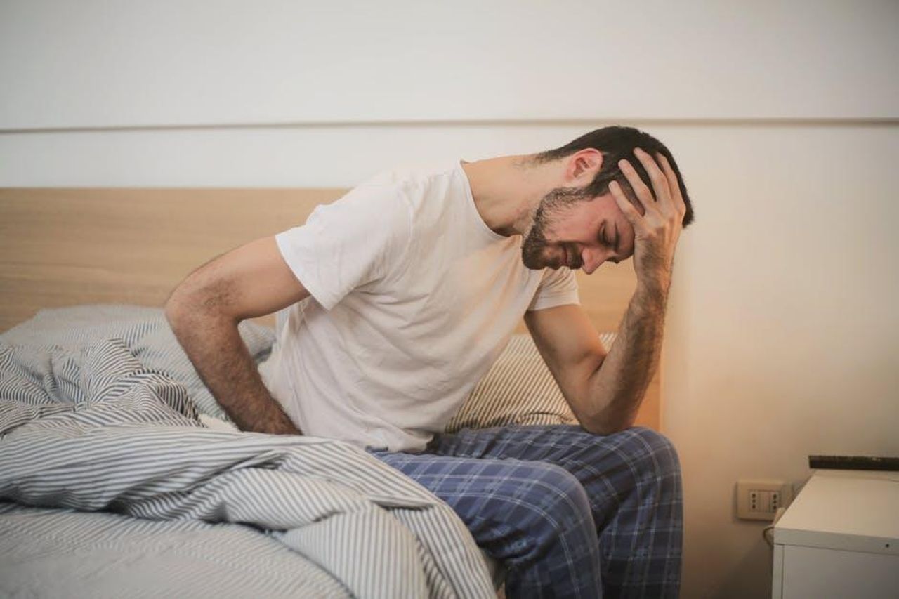 Alberto_turbato_da_Luca_X3C6W3RfKc - Confidenze24 Source: Andrea Piacquadio - pexels - A young man in pajamas holding his head, sitting on a bed, appears to be experiencing a headache.