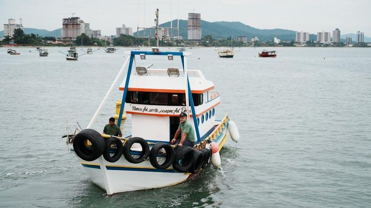 Alfredo_ritorna_a_Milano_anticipazioni_Il_Paradiso_delle_signore_del_18_febbraio_PG8FLz88gw - Confidenze24 Source: Aleson Padilha - pexels - A vibrant fishing boat returns to dock with scenic city skyline in the background, capturing coastal life.
