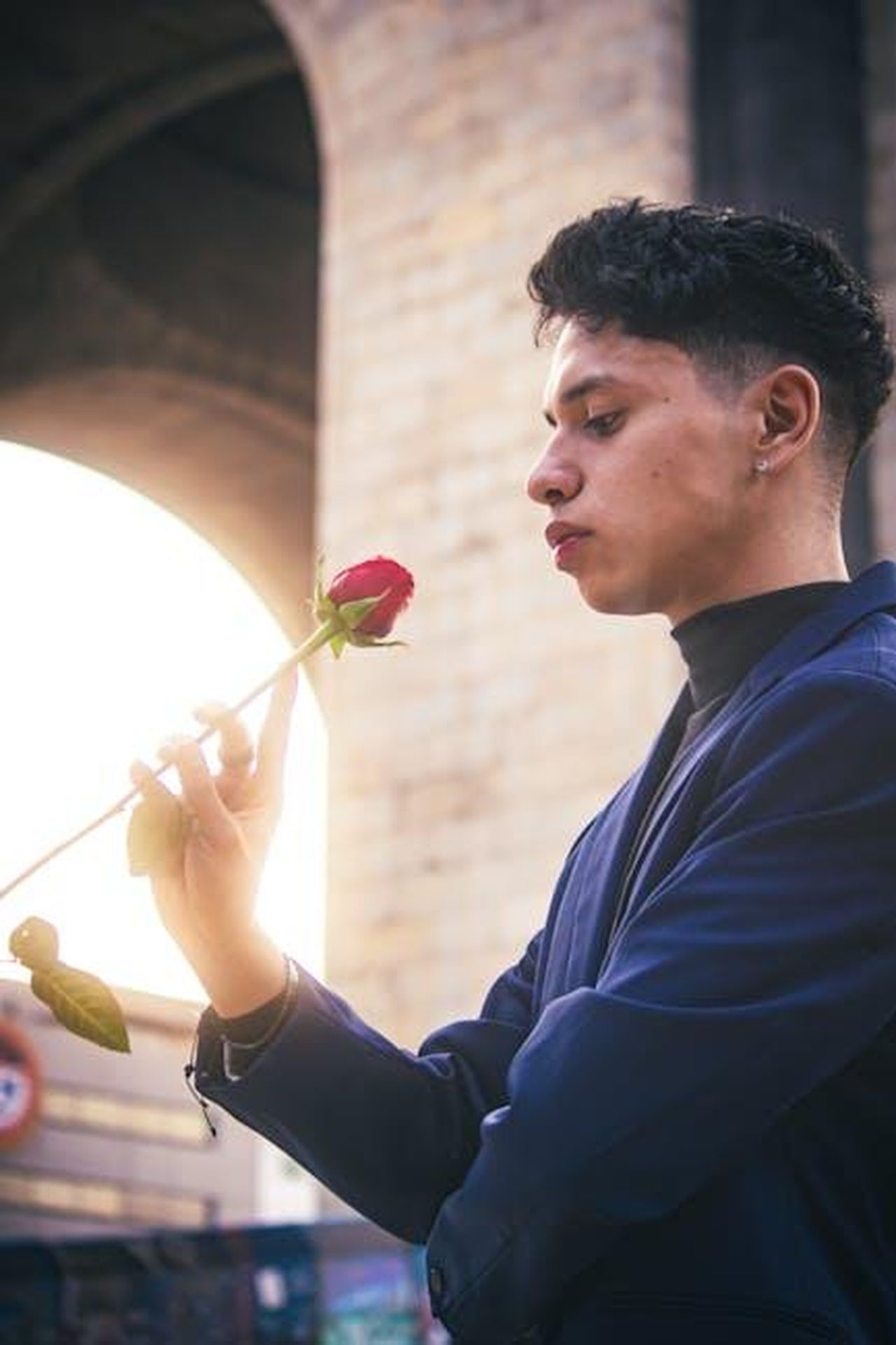 Ammirazione_a_distanza_DrDUA0nKHB - Confidenze24 Source: Moisés Fonseca - pexels - Young man in blue suit admiring a red rose outdoors during sunset in Ciudad de México.