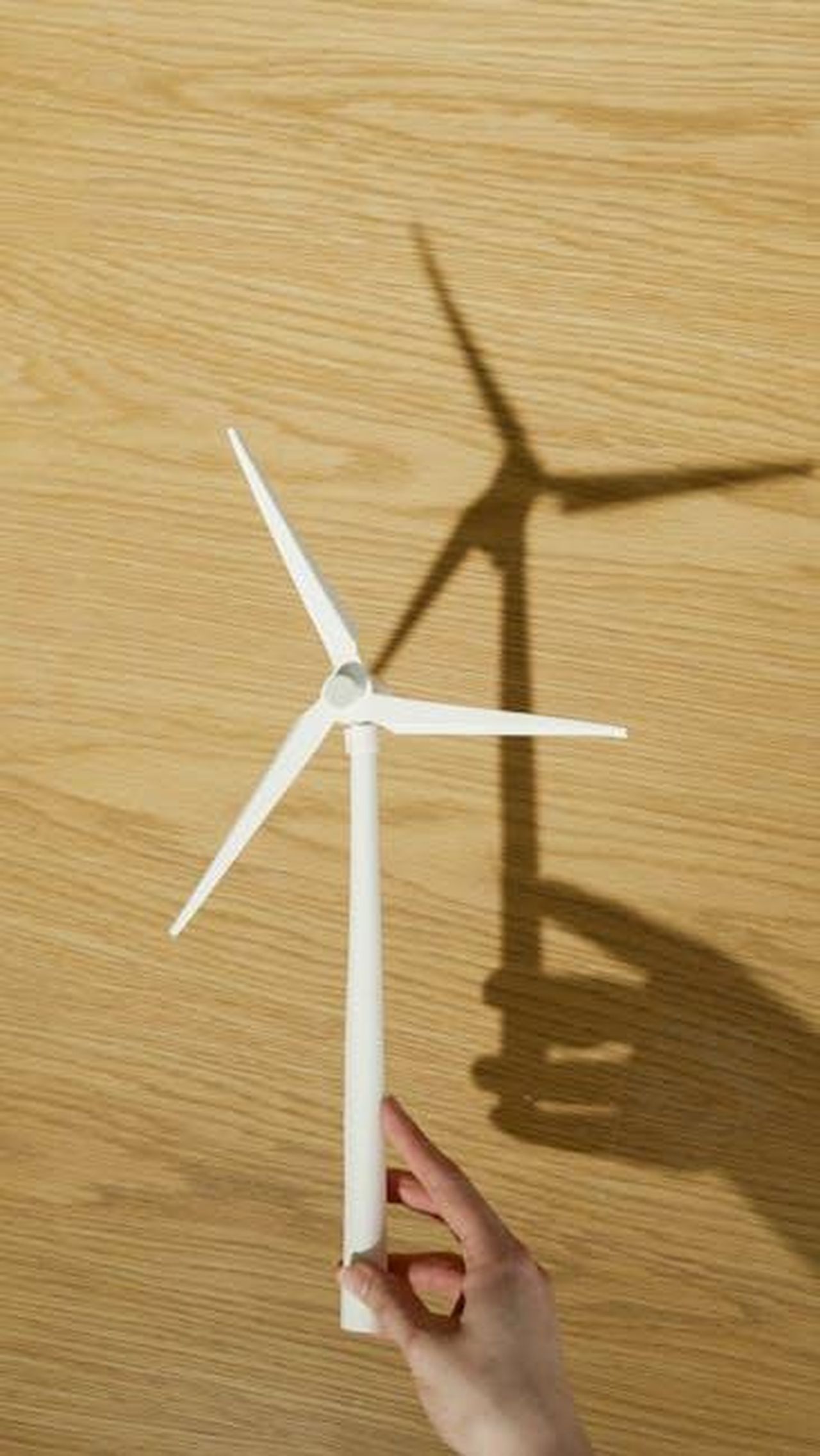 Ariete_Energia_vulcanica_22Ybpjecx9 - Confidenze24 Source: Artem Podrez - pexels - Close-up of a hand holding a small wind turbine model casting a shadow on a wooden surface.