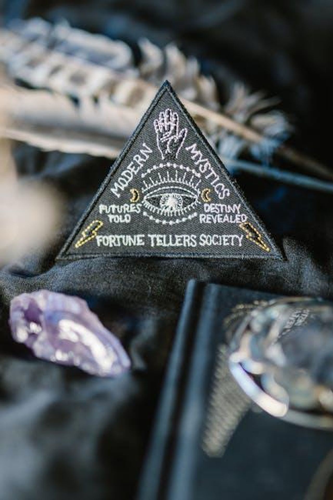 Ariete_intrappolati_in_un_loop_temporale_7MnW1df2Vq - Confidenze24 Source: RDNE Stock project - pexels - A mystical triangle patch with fortune-telling themes surrounded by crystals and feathers on dark background.