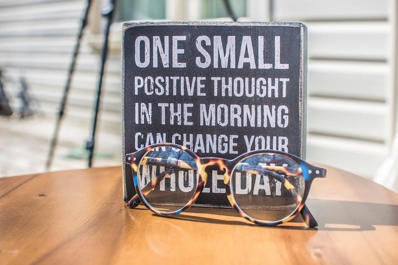 Bilancia_Energia_positiva_rcC63JoZdw - Confidenze24 Source: Binti Malu - pexels - Eyeglasses resting on a table in front of a motivational quote sign, emphasizing positivity.