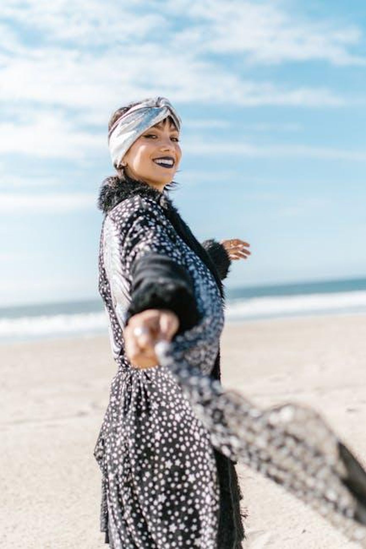 Bilancia_credere_nei_miracoli_ZUhrNo9Muo - Confidenze24 Source: RDNE Stock project - pexels - Joyful woman enjoying a sunny day at the beach, wearing stylish polka dot dress and headscarf.