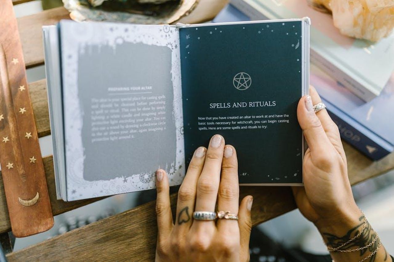 Cancro_22_giugno__22_luglio_c3JFrWhVsO - Confidenze24 Source: RDNE Stock project - pexels - Close-up of hands holding an open book about spells and rituals, featuring a pentagram symbol.