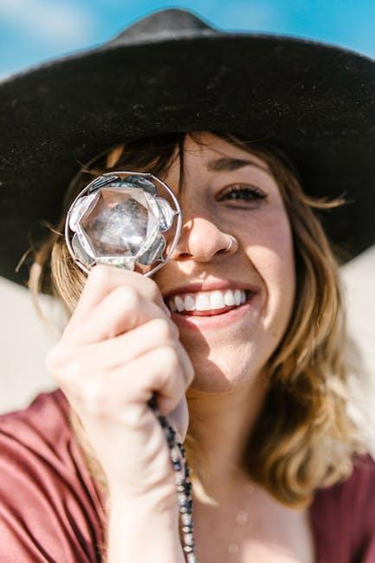 Cancro_determinato_al_lavoro_2Ho1GWnc9e - Confidenze24 Source: RDNE Stock project - pexels - A smiling woman with a hat holds a prism crystal outdoors in sunlight.