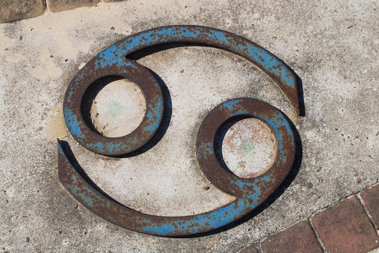 Cancro_riscatto_e_rinascita_3B3JggbZrZ - Confidenze24 Source: Antonio Garcia Prats - pexels - Close-up of a rusted Cancer zodiac symbol on a concrete wall.