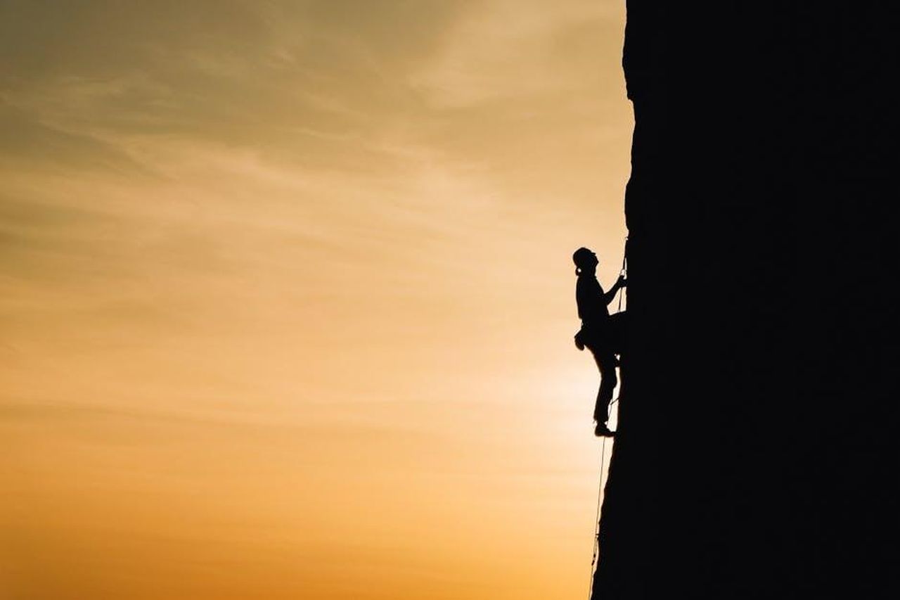 Capricorno_Determinazione_e_pragmatismo_b67eFzbZuf - Confidenze24 Source: Анна Рыжкова - pexels - A silhouette of a rock climber scaling a steep cliff during sunset in Russia, showcasing determination and adventure.