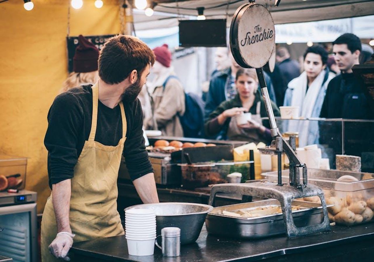 Cibo_e_bevande_cosa_aspettarsi_N2qYLN45jo - Confidenze24 Source: Clem Onojeghuo - pexels - Dynamic scene of a street food vendor working in a busy market, engaging with diverse customers.