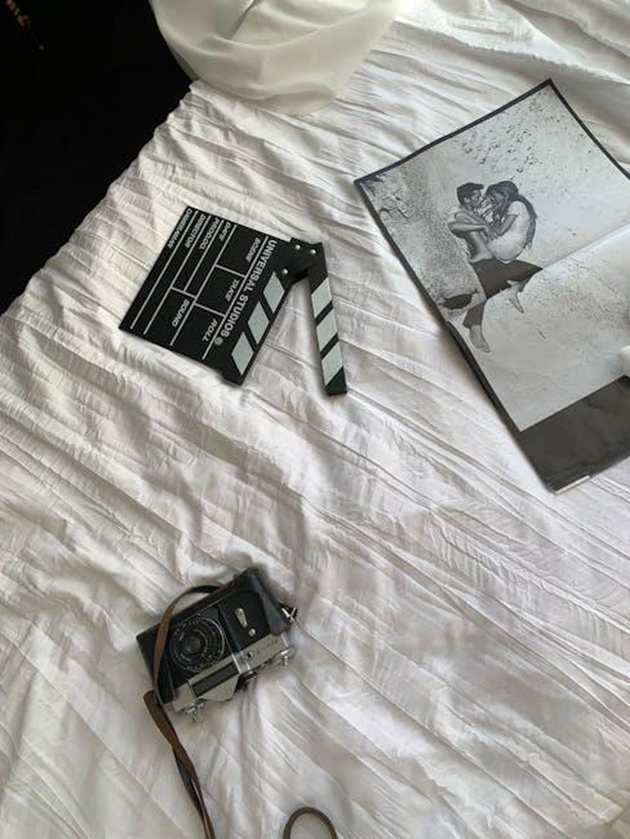 Cinema_giornalismo_e_cultura_protagonisti_eAVrO9mtuc - Confidenze24 Source: Tatyana Doloman - pexels - Black and white photo with vintage camera and film slate on a white sheet bed.