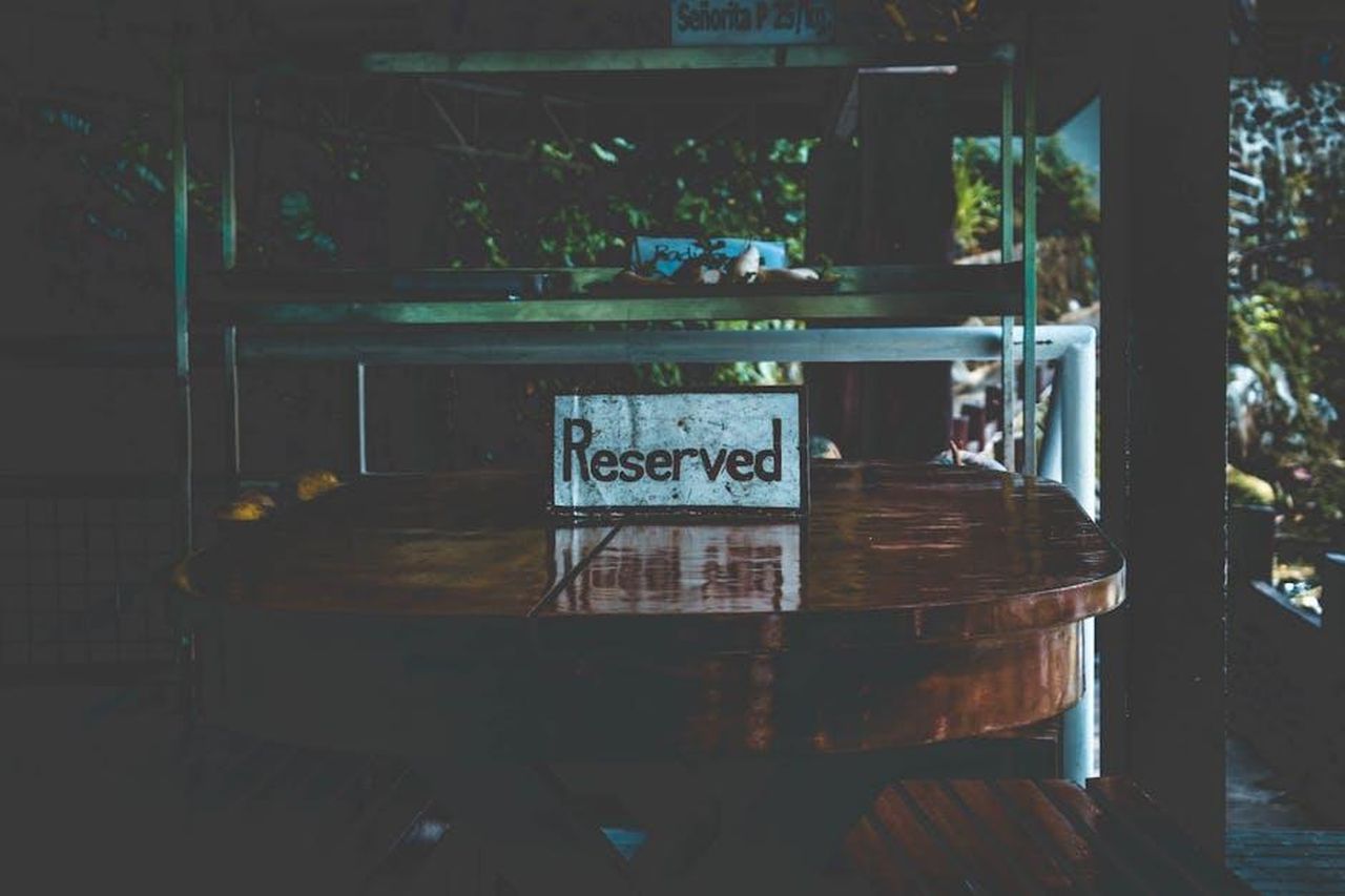 Come_prenotare_un_tavolo_con_Donnie_Wahlberg_kpB7fBwBos - Confidenze24 Source: iOnix08 - pexels - A dimly lit table with a reserved sign, set in an outdoor environment creating a moody atmosphere.