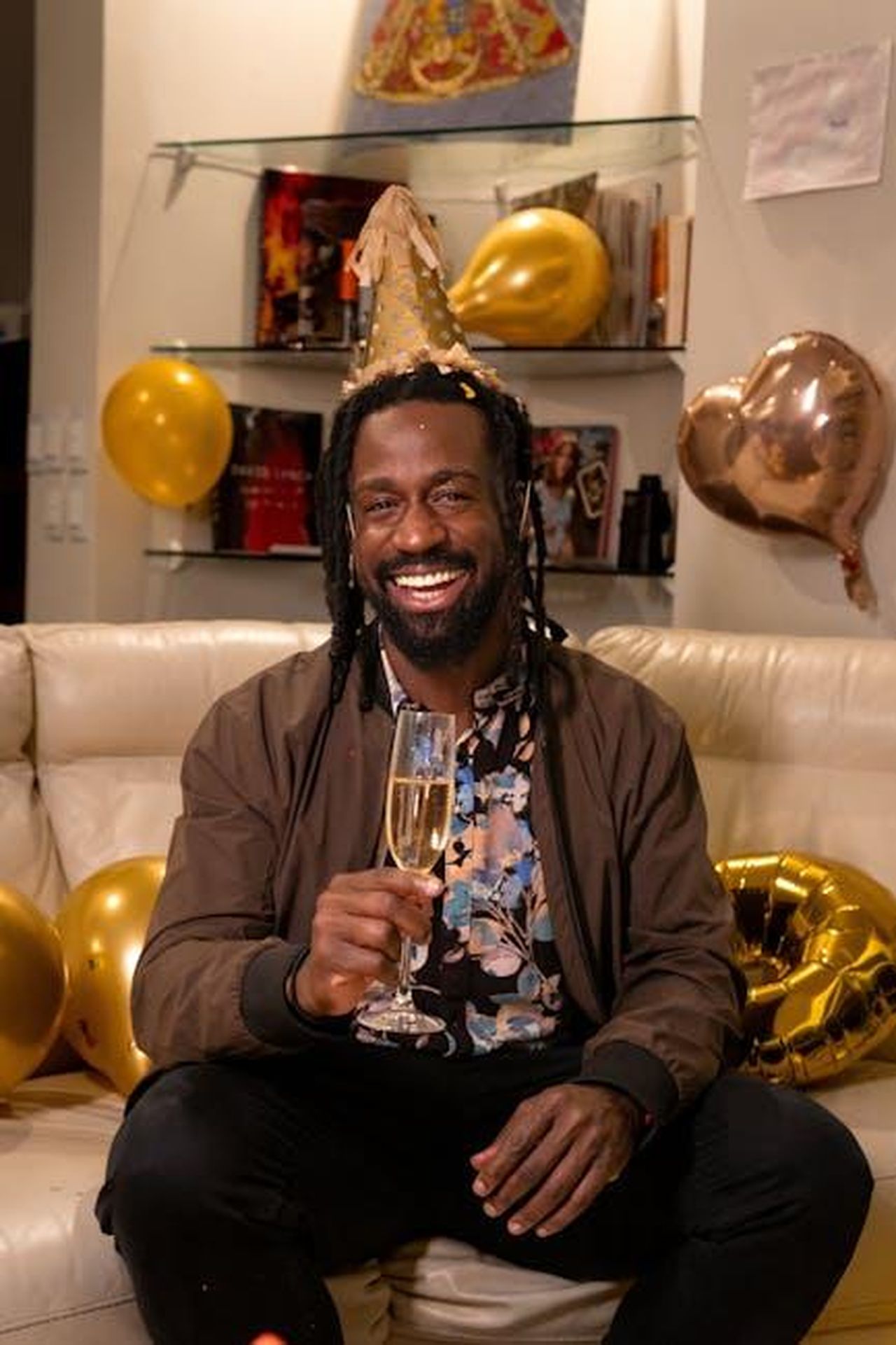 Commenti_dei_follower_sulla_festa_dxCEMmbZcJ - Confidenze24 Source: Diana Reyes - pexels - Smiling man wearing party hat, holding champagne amidst festive decor.