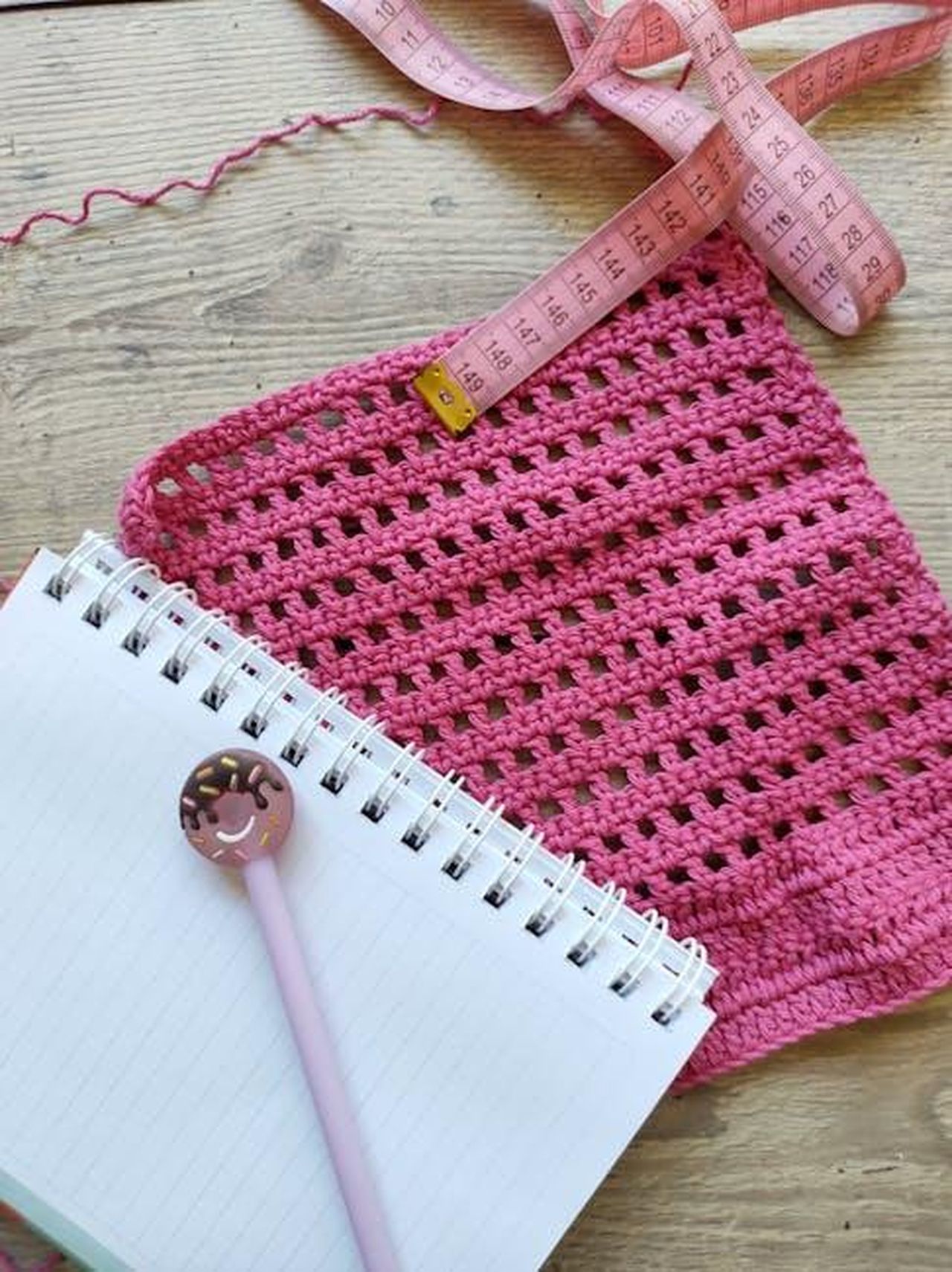Critiche_dei_fan_sui_buchi_di_trama_h06y8bRvyv - Confidenze24 Source: Sandra Garmendia - pexels - A pink crochet sample with a tape measure and notebook, perfect for creative DIY projects.