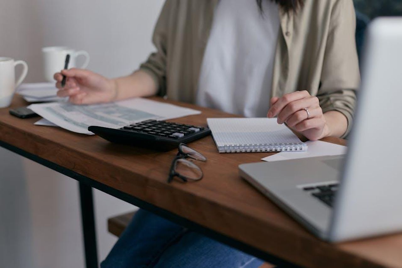 Damiano_continua_ad_avere_problemi_in_ufficio_con_Gallo_ton2mydNg4 - Confidenze24 Source: Mikhail Nilov - pexels - A woman manages finances at home, using a laptop and calculator on a wooden desk.