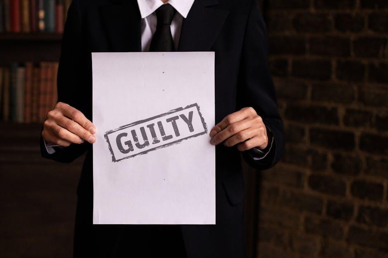 Dichiarazioni_di_Caesar_McDowell_su_Tory_Lanez_TB1MT2leoG - Confidenze24 Source: KATRIN BOLOVTSOVA - pexels - A businessman in a formal suit holding a sign with the word 'GUILTY.'