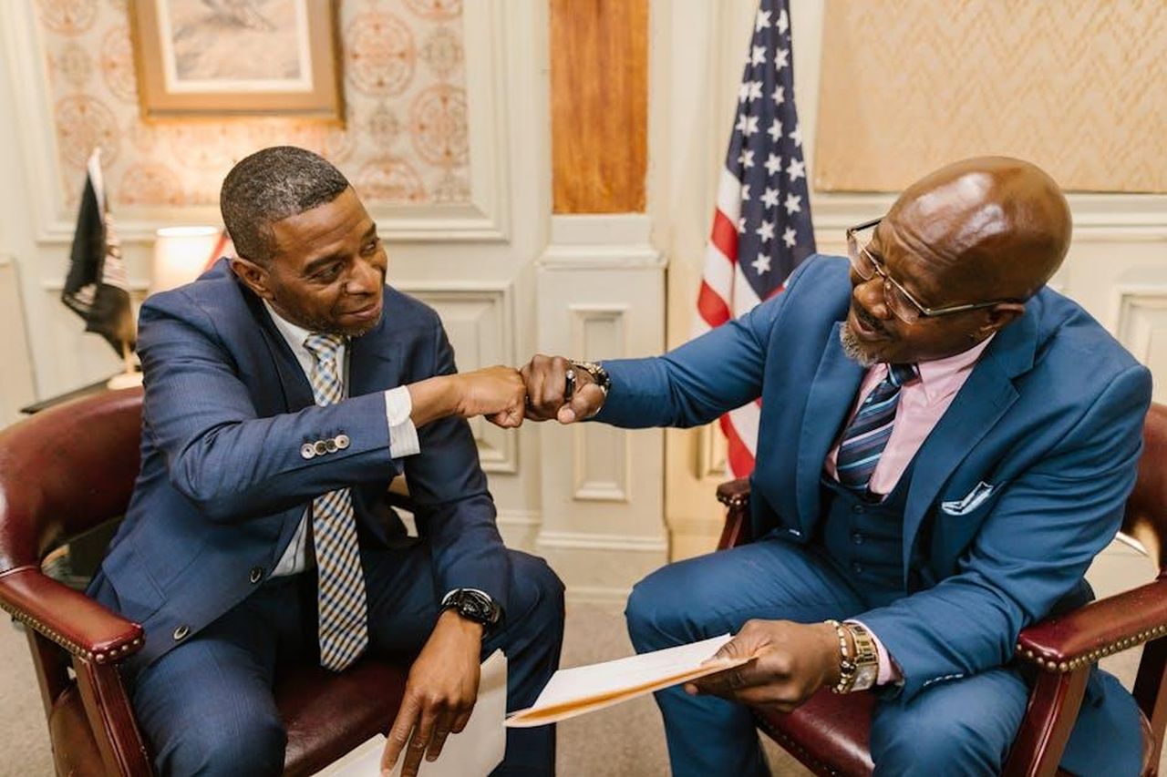 Divorzio_di_Helen_George_Yl2oKqOMUp - Confidenze24 Source: RDNE Stock project - pexels - Two businessmen in suits engage in a friendly fist bump in a formal office environment.