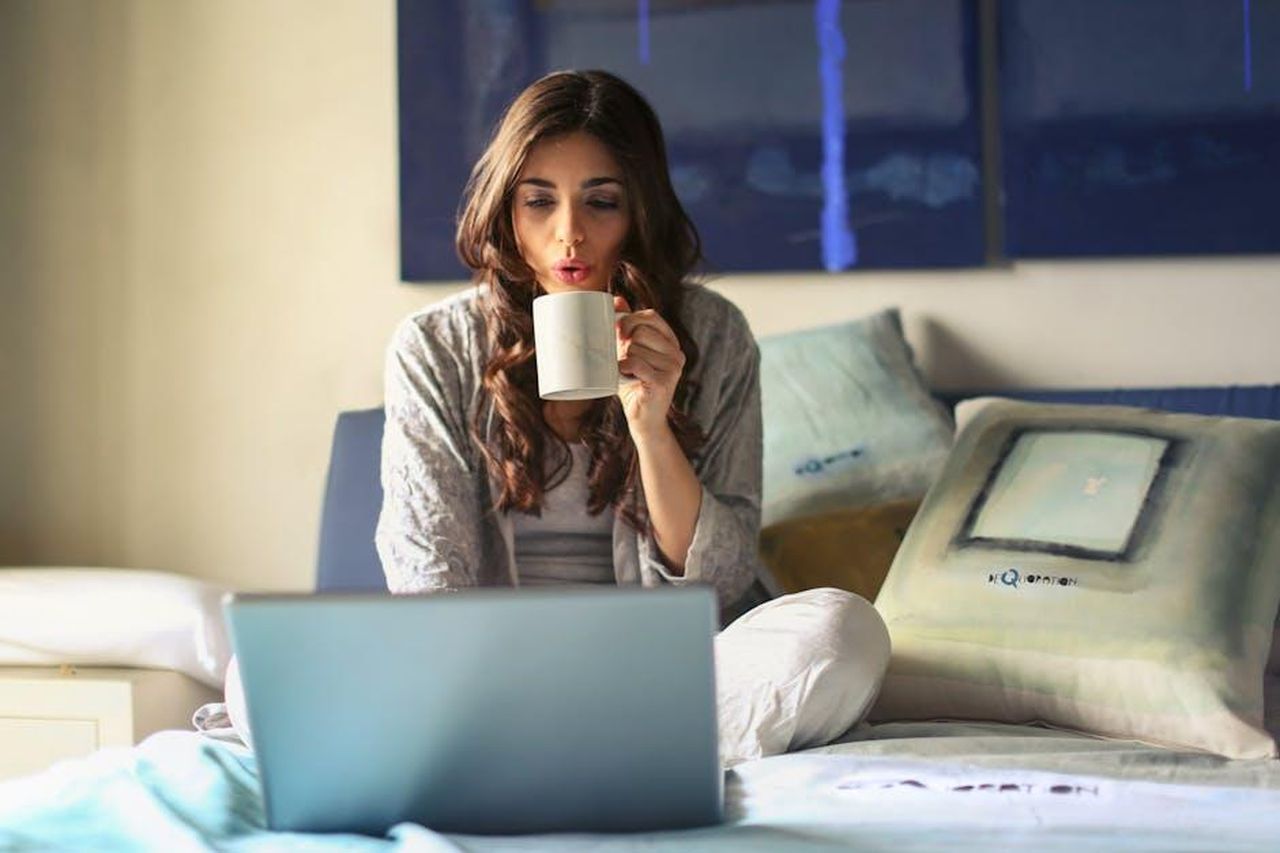 Dove_rivedere_le_puntate_di_Beautiful_FjKQi1kDCf - Confidenze24 Source: Andrea Piacquadio - pexels - A woman enjoying coffee while working from home in a cozy bedroom setting with a laptop.