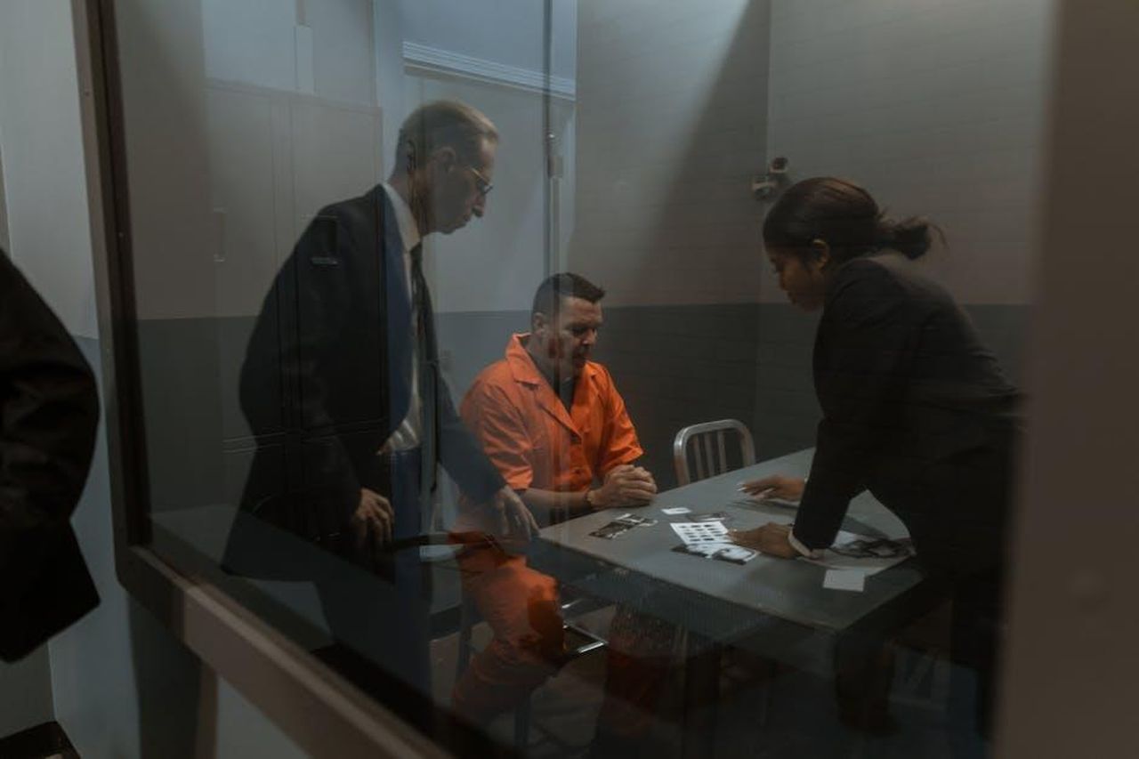 Faccia_a_faccia_tra_Stefania_e_Zeudi_kT6jsj11dd - Confidenze24 Source: RDNE Stock project - pexels - A tense interrogation in progress with a handcuffed inmate and two officers in a prison room.