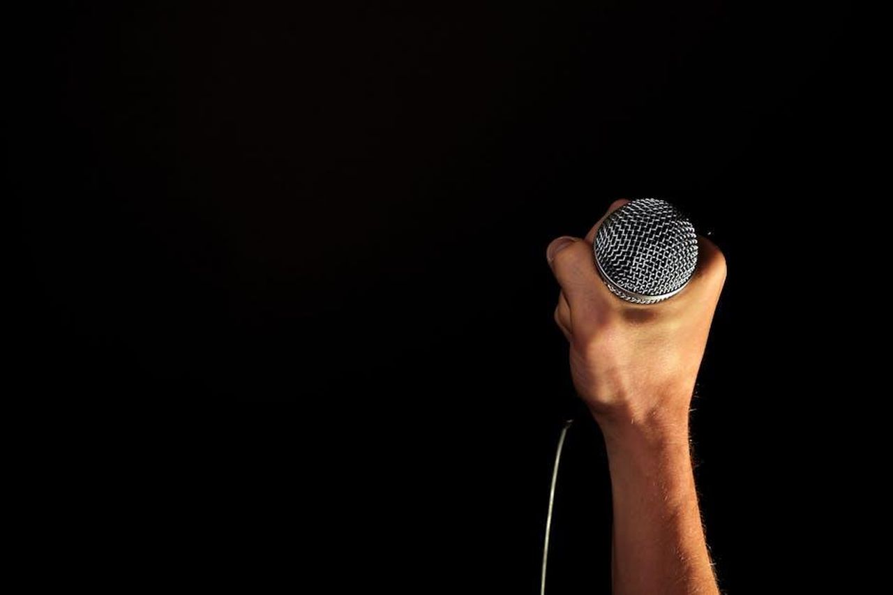Favoriti_per_la_vittoria_finale_vKHRHRRSbw - Confidenze24 Source: Pixabay - pexels - Close-up of a hand firmly gripping a microphone against a dark backdrop.