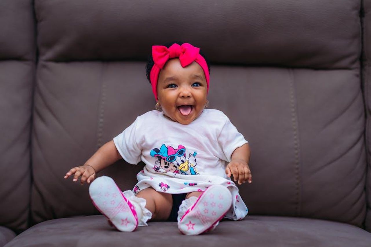 Ges_era_il_parrucchiere_e_amico_di_Kylie_GiGuYMYzam - Confidenze24 Source: Hassan Mukhtar - pexels - Cute baby with pink headband smiling joyfully on a sofa.