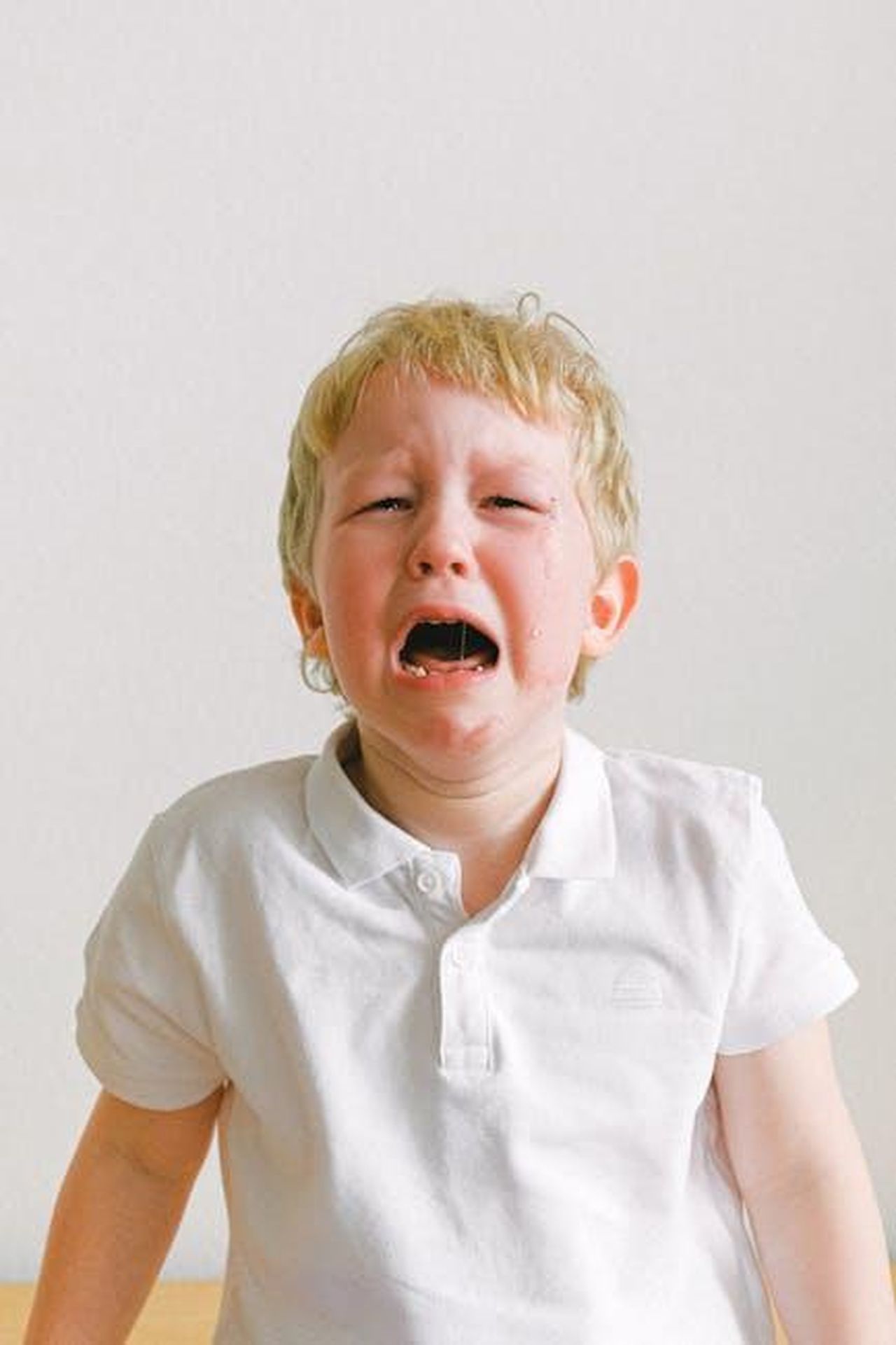Guzide_aveva_notato_che_qualcosa_tormentava_Sezai_k3QvwMK6IR - Confidenze24 Source: Anna Shvets - pexels - A young child crying, wearing a white shirt, showing strong emotions indoors.