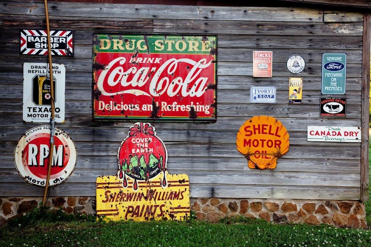 Harrison_Ford_e_Jessica_Williams_una_coppia_affiatata_RrU4yWK6Y4 - Confidenze24 Source: Pixabay - pexels - Collection of vintage advertising signs on rustic wooden wall showcasing classic brands.