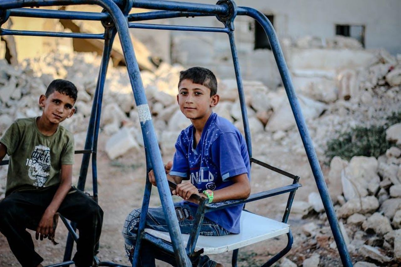 Hope_cerca_di_ricostruire_la_sua_vita_dCNDguKRuv - Confidenze24 Source: Ahmed akacha - pexels - Two boys sitting on a swing outdoors amidst rubble in Idlib, Syria, depicting life resilience.