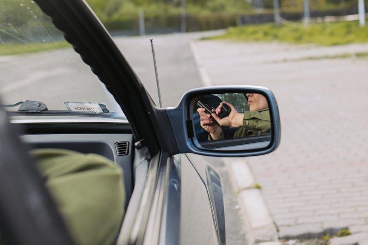 I_Colpi_Di_Scena_E_Le_Aspettative_Per_Duplicity_X1flwfXZw1 - Confidenze24 Source: KoolShooters - pexels - A person with a gun captured in the car's side mirror, suggesting a mysterious scenario.
