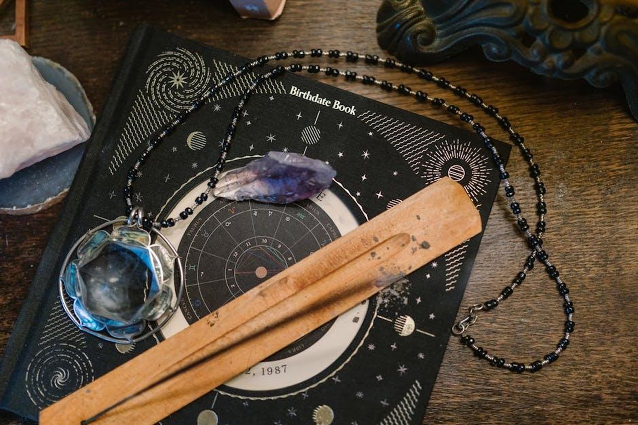 I_primi_segni_dello_zodiaco_bZEawBVYPq - Confidenze24 Source: RDNE Stock project - pexels - Astrology-themed flat lay featuring a birthdate book, crystals, and necklace on a wooden surface.