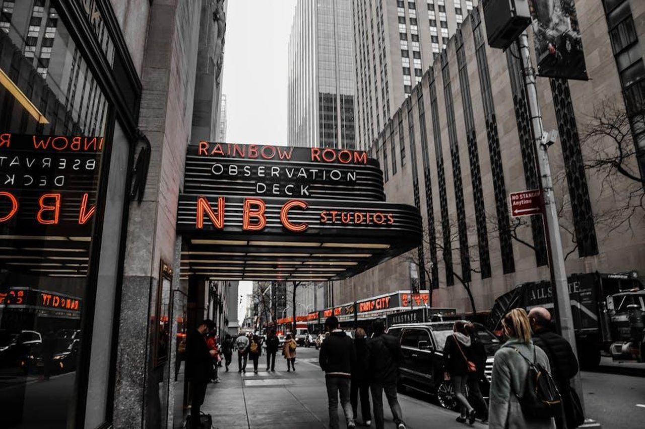 Il_Futuro_di_Lester_Holt_in_NBC_oXvMQshxmf - Confidenze24 Source: Gela delrose - pexels - Street view of NBC Studios at Rockefeller Center, New York City, with people walking and iconic signage visible.
