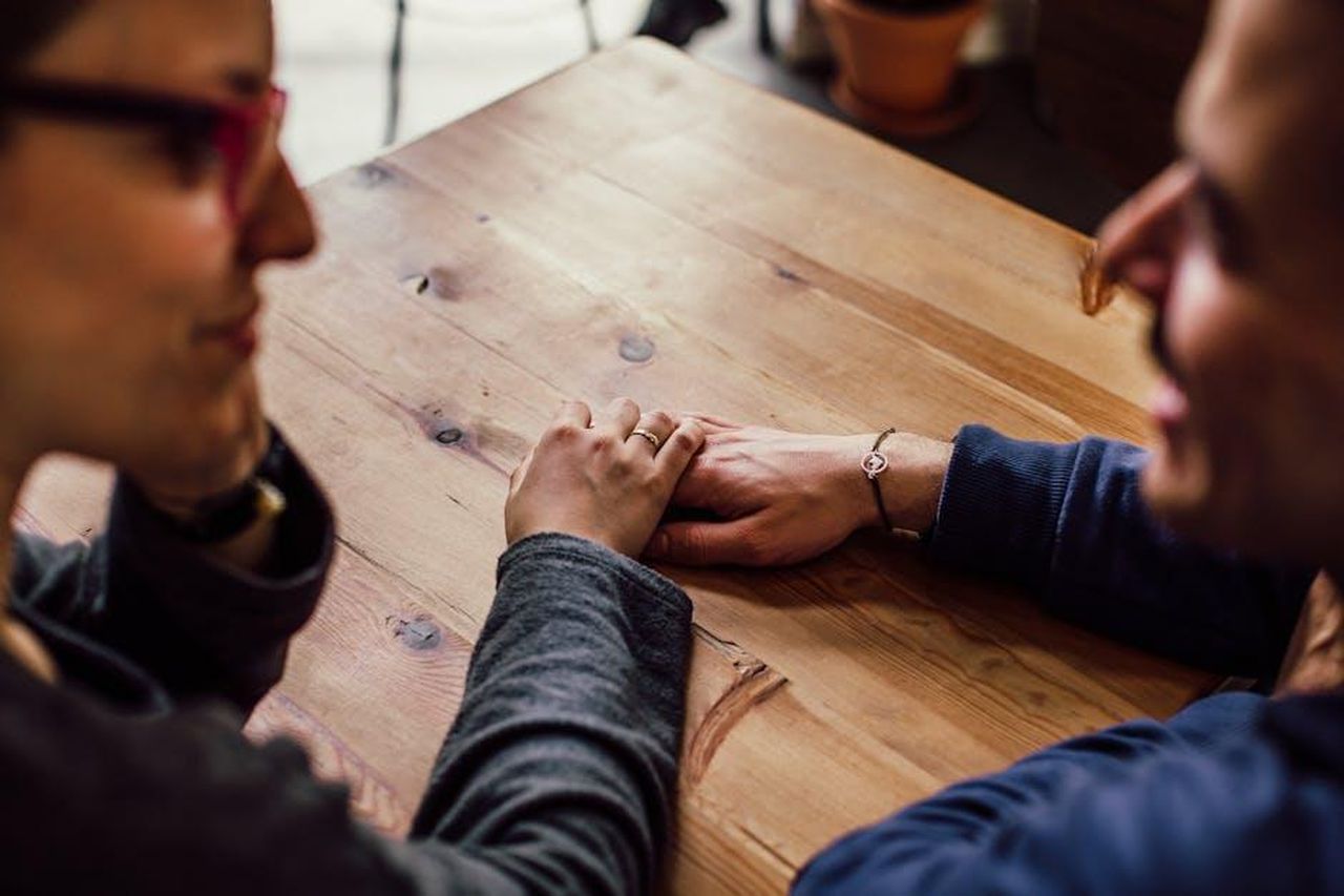Il_Supporto_di_Prince_Harry_iv1a62siTR - Confidenze24 Source: Juan Pablo Serrano - pexels - A couple shares a romantic moment holding hands across a wooden table indoors.