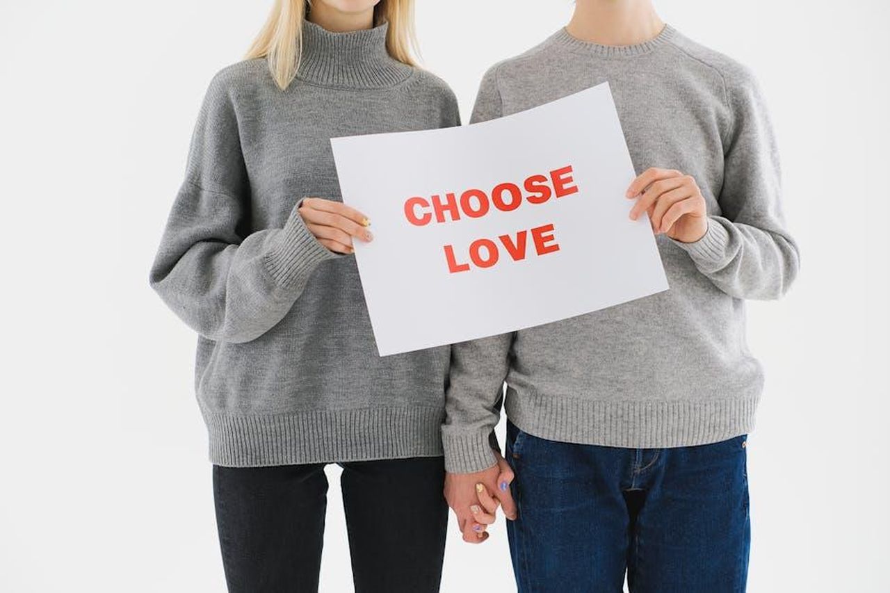 Il_chiarimento_al_risveglio_DeUGcK17YM - Confidenze24 Source: Anna Shvets - pexels - A couple in grey sweaters holding a 'Choose Love' sign, promoting love and unity.