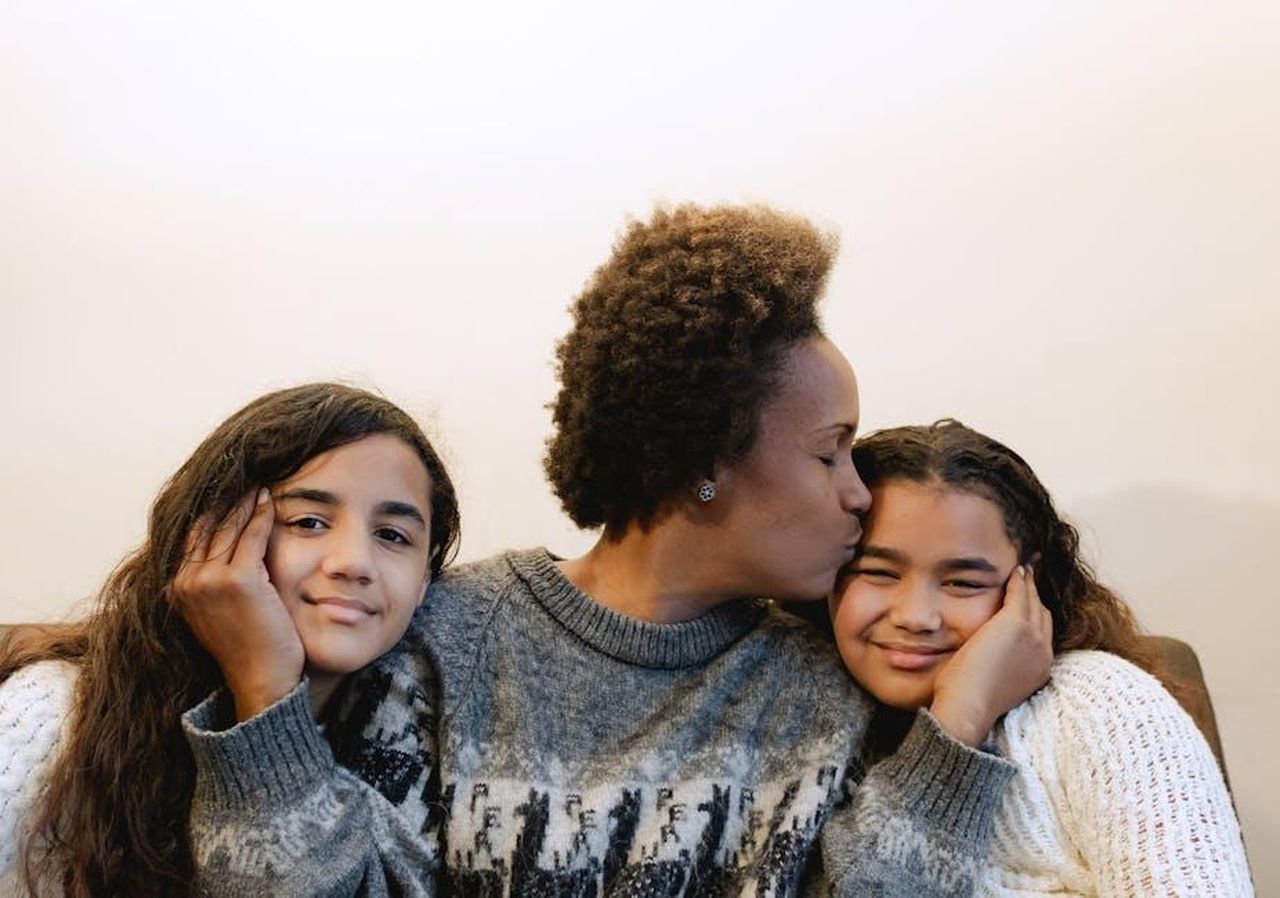 Il_legame_tra_Zaya_e_Gabrielle_un_supporto_incondizionato_EWakcgWSsV - Confidenze24 Source: Olha Ruskykh - pexels - A joyful mother kissing her smiling daughters indoors, capturing love and family warmth.