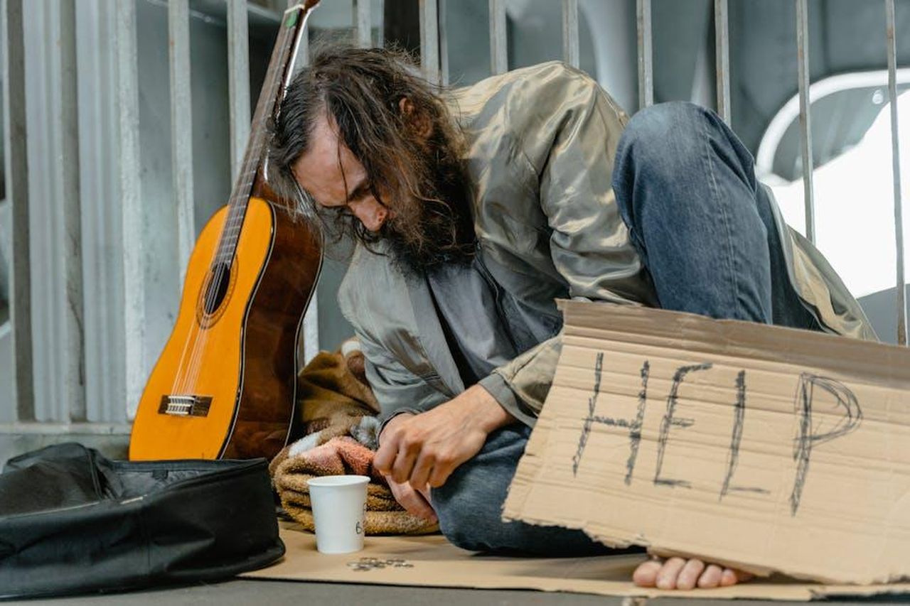Il_messaggio_dellalbum_e_le_donazioni_KZRAOfQBvb - Confidenze24 Source: MART PRODUCTION - pexels - A homeless man sits with a guitar and a help sign on a city street.