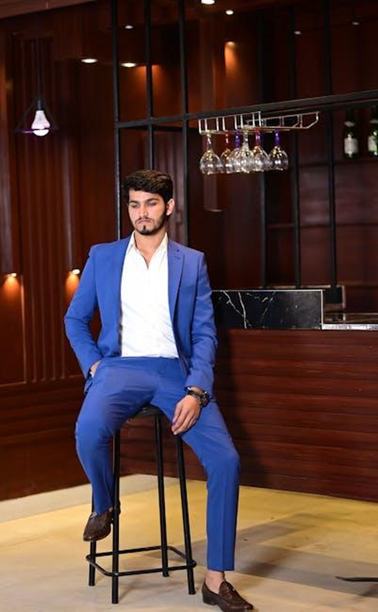 Il_parere_del_maggiordomo_Grant_Harrold_sulla_relazione_tra_William_e_Harry_gwJB3M0PRc - Confidenze24 Source: Hamza Awan - pexels - A stylish man in a blue suit sits confidently at a luxurious bar setting indoors.