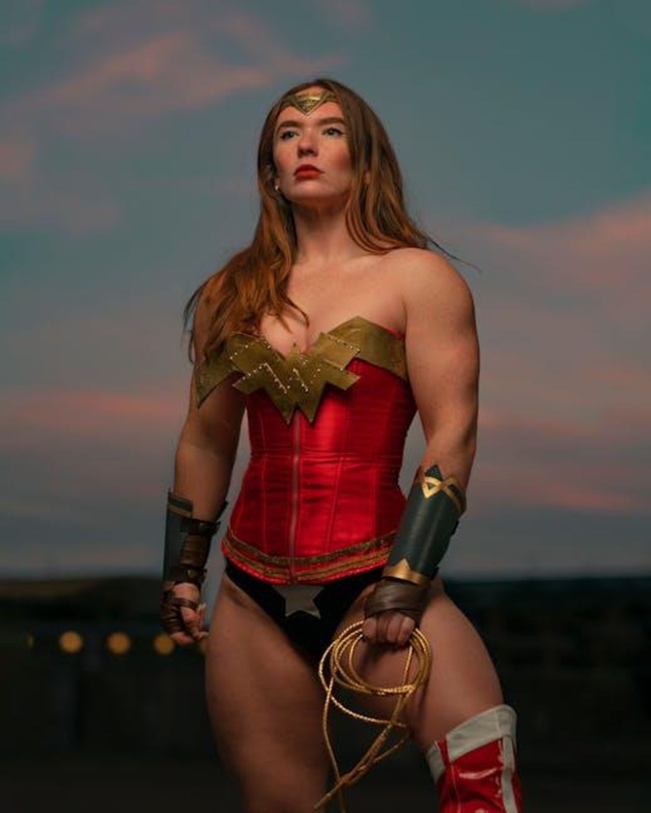 Il_passato_di_Hewitt_con_Diana_K8gK6lRVjt - Confidenze24 Source: Roy Reyna - pexels - A strong woman dressed in superhero costume poses outdoors against a dramatic sunset sky.